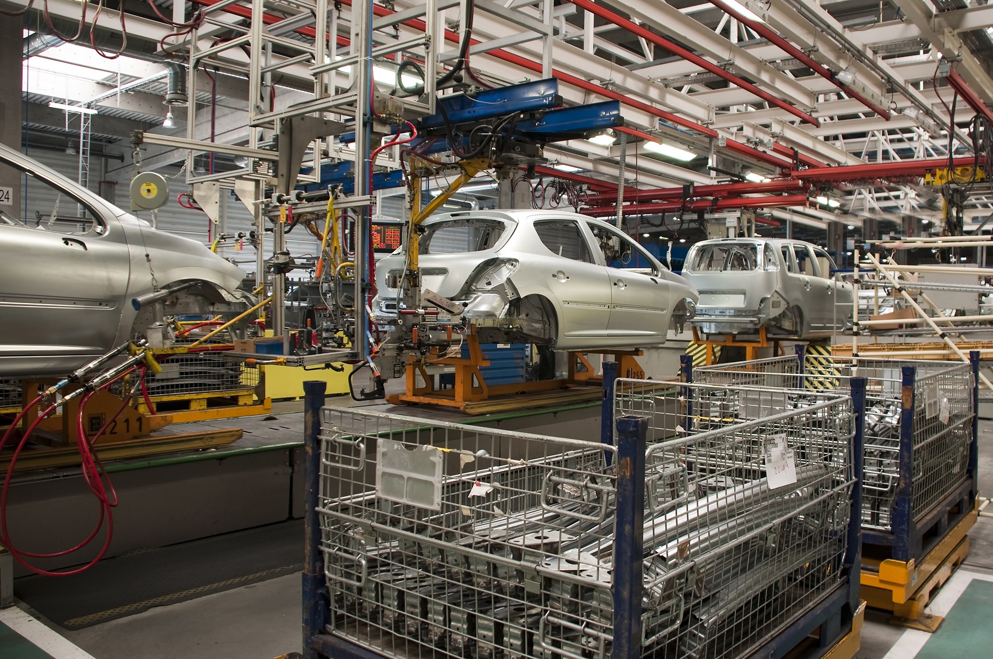 Automotive assembly line showcasing several car bodies on stations, with robotic arms and metal frames in background, emphasizing industrial manufacturing.
