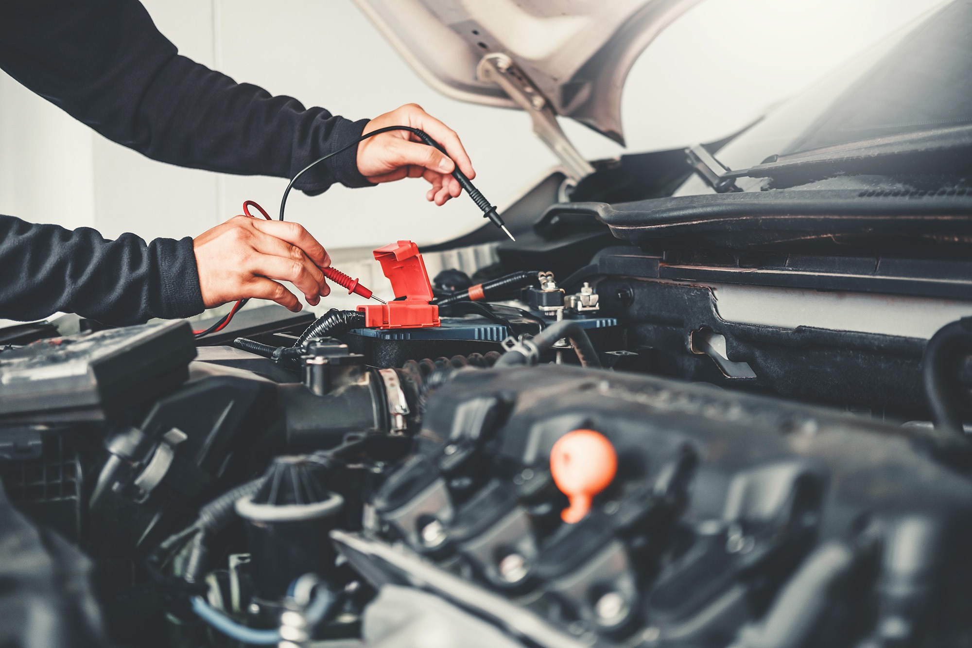 A person tests a car battery using multimeter probes, illustrating automotive maintenance and diagnostics in progress.
